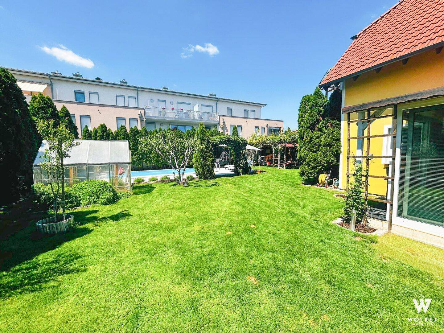Umfangreicher Garten mit Rasenfläche, Pool und einem charmanten Haus mit rotem Dach.