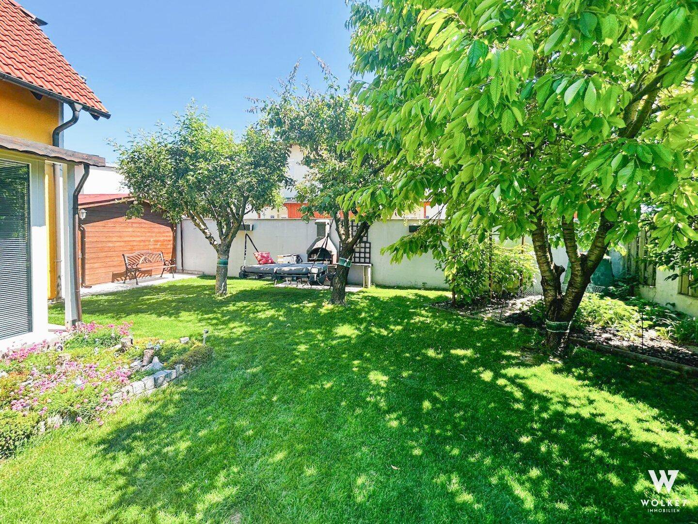 Schattiger Gartenbereich mit großen Bäumen, Schaukel und Grillstelle für entspannte Stunden.