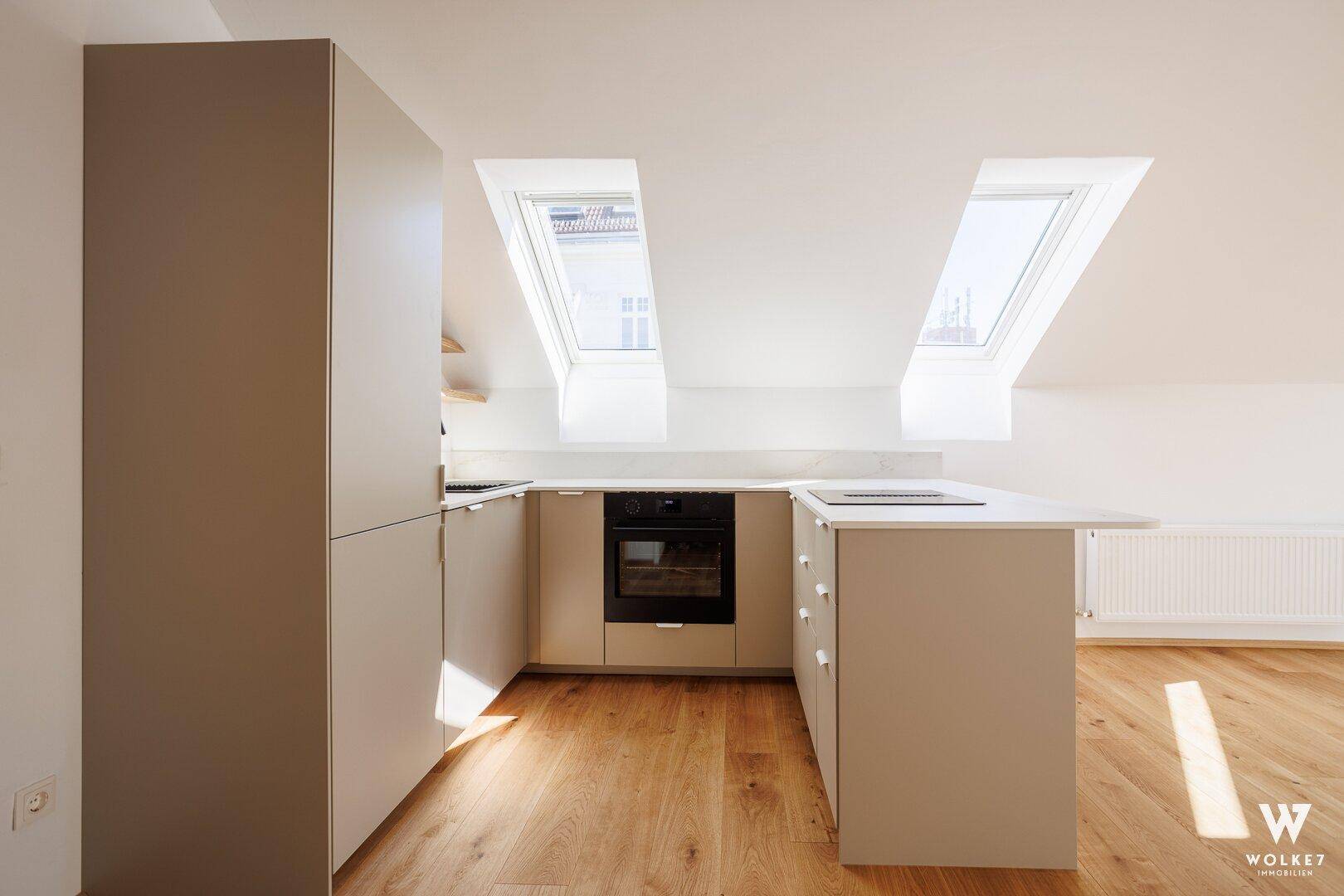 Moderne Küchenzeile im Dachgeschoss mit integriertem Backofen, hellen Schränken und Dachfenstern.