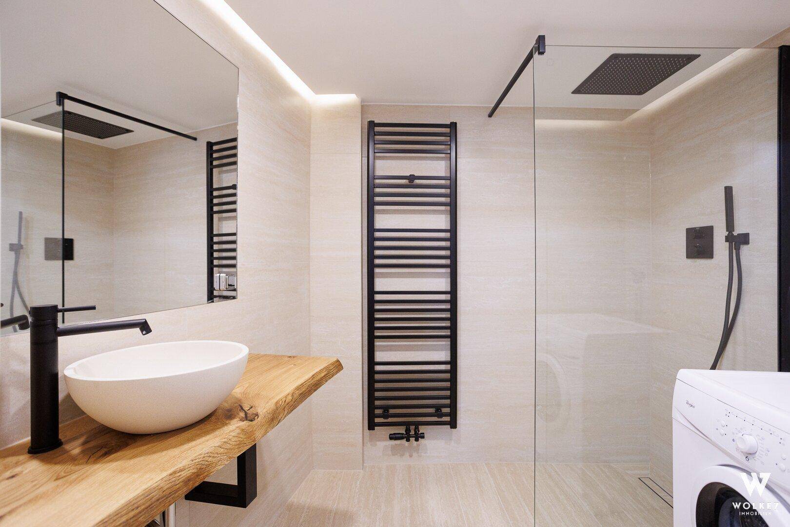 Modernes Badezimmer mit begehbarer Dusche, Holzwaschtisch, beheiztem Handtuchhalter und Waschmaschine.