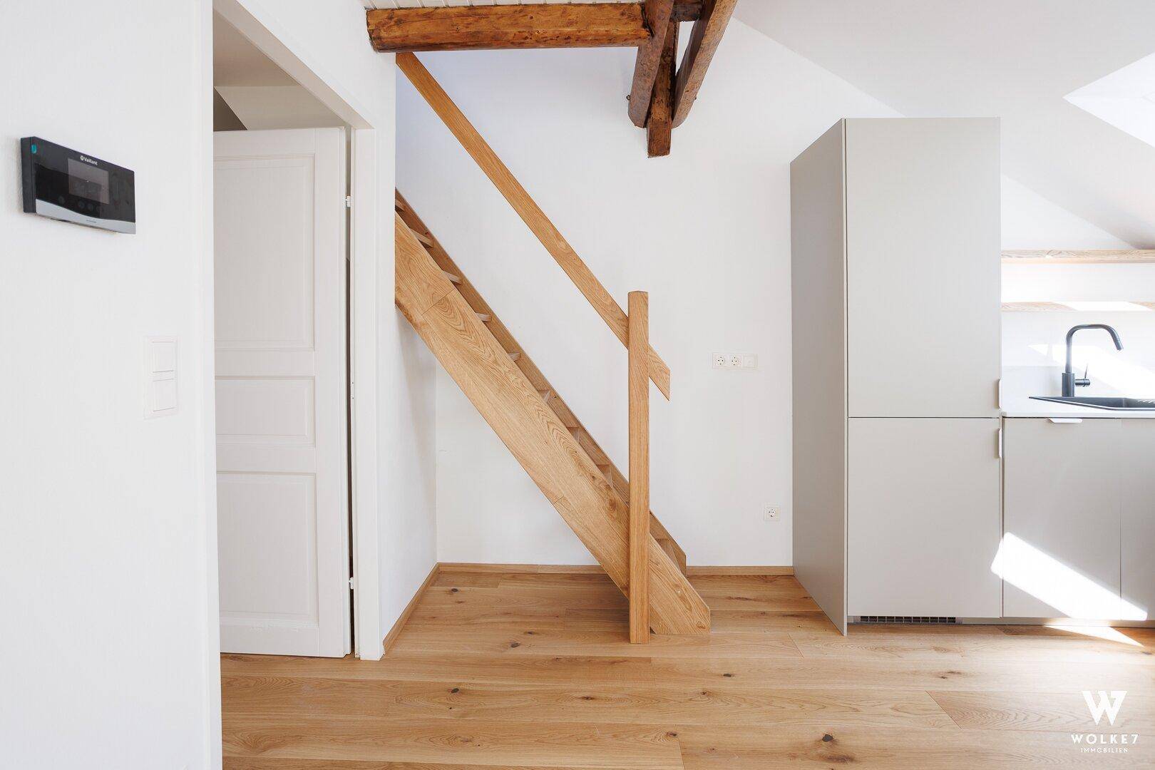Offener Wohnbereich mit Holztreppe, moderner Küchenzeile und sichtbarem Holzbalken.