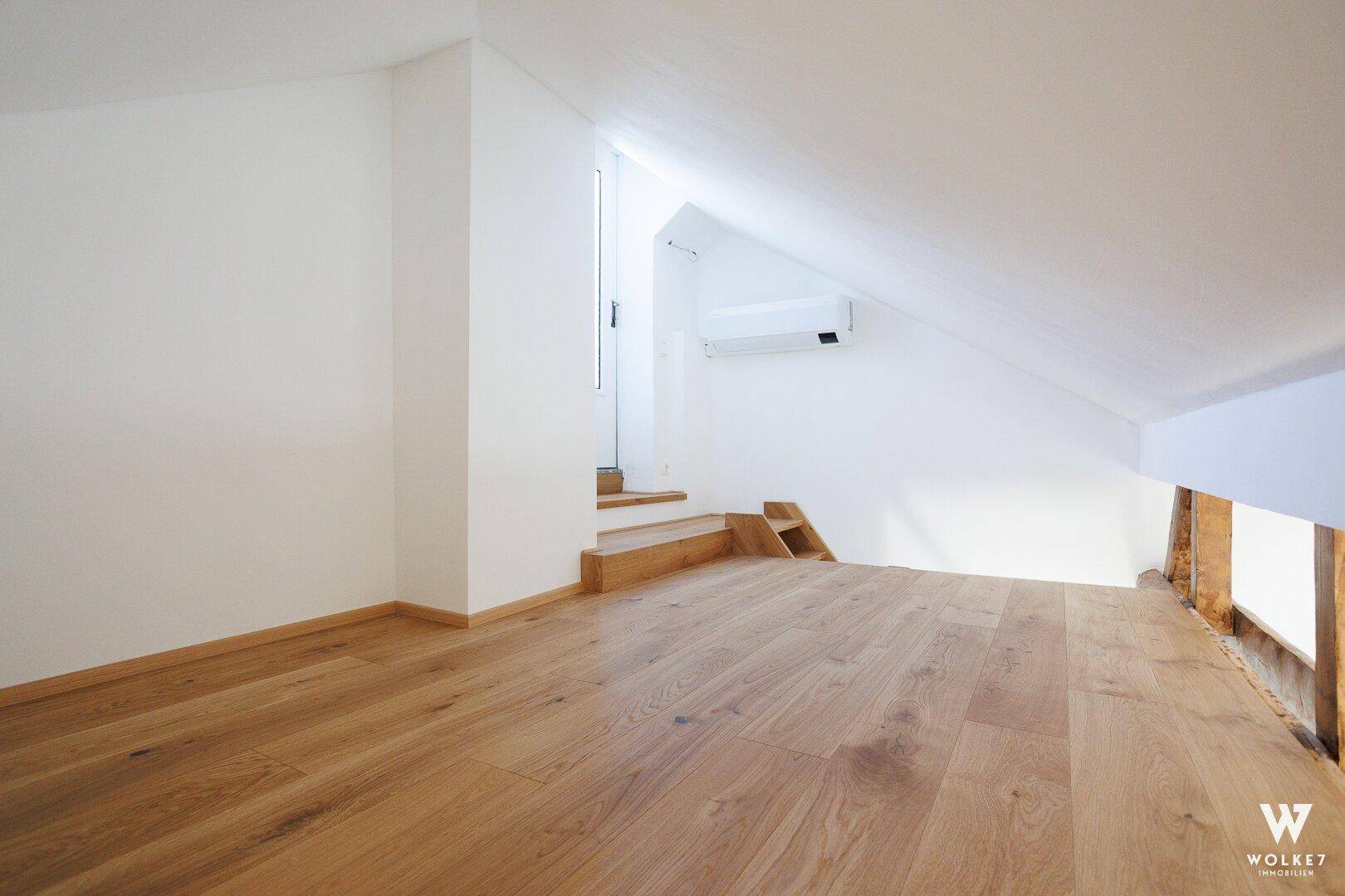 Geräumiger Dachbodenraum mit Holzboden, Klimaanlage und Treppe zu einer oberen Ebene.