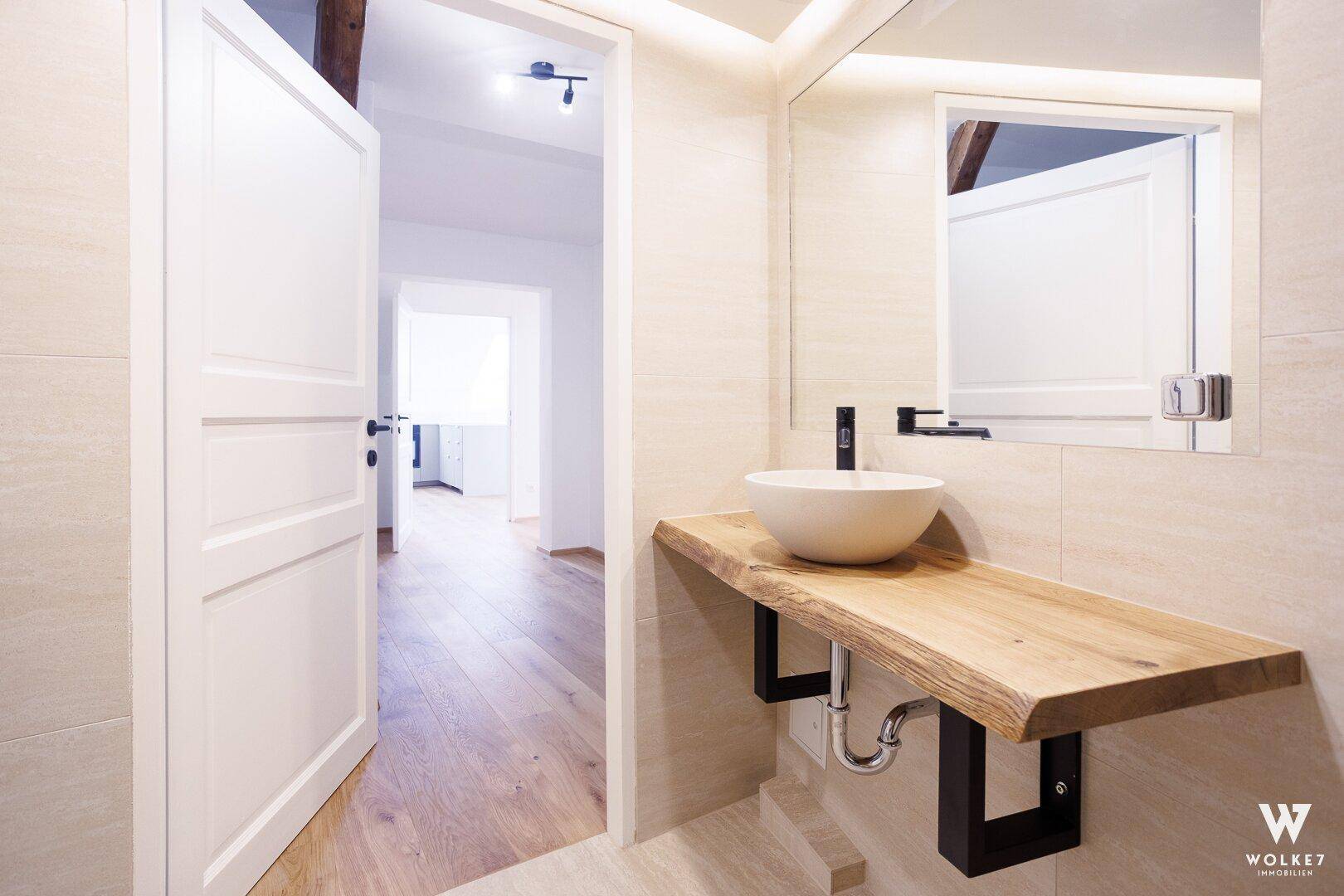 Elegantes Badezimmer mit modernem Waschbecken auf Holzplatte und großem Spiegel.