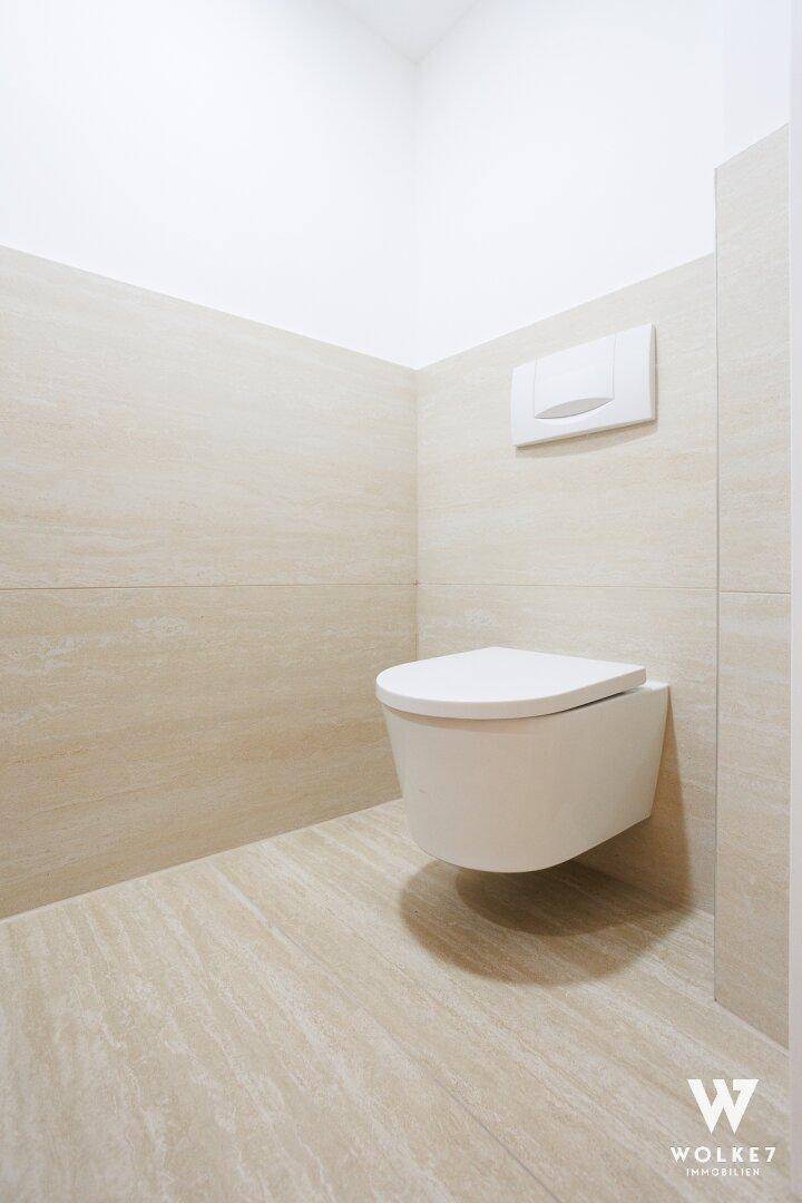 Modernes WC mit wandhängender Toilette und hellen Fliesen an Wänden und Boden.