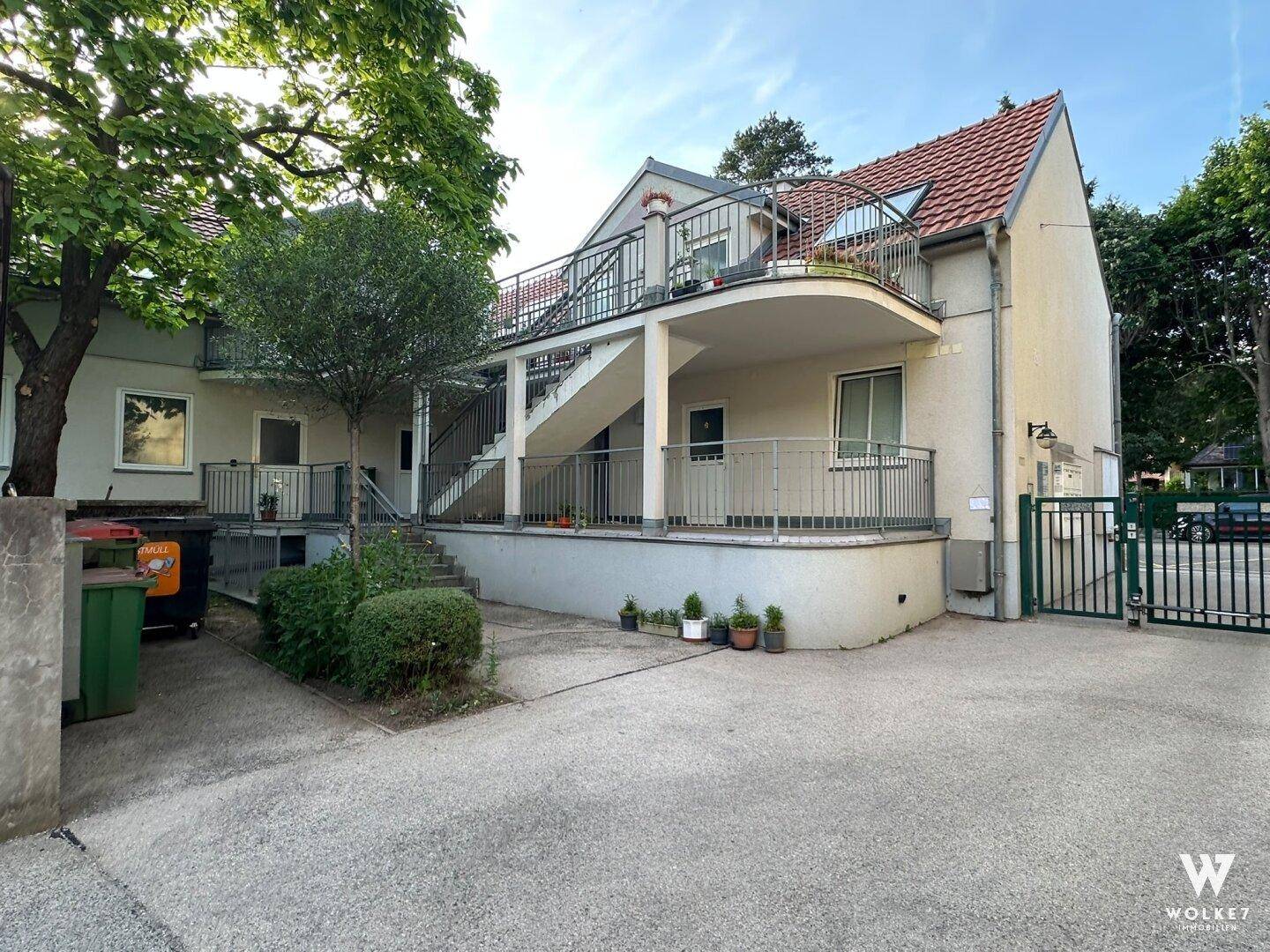 Rückansicht des Gebäudes mit Außentreppe, mehreren Balkonen und einem kleinen Hofbereich.