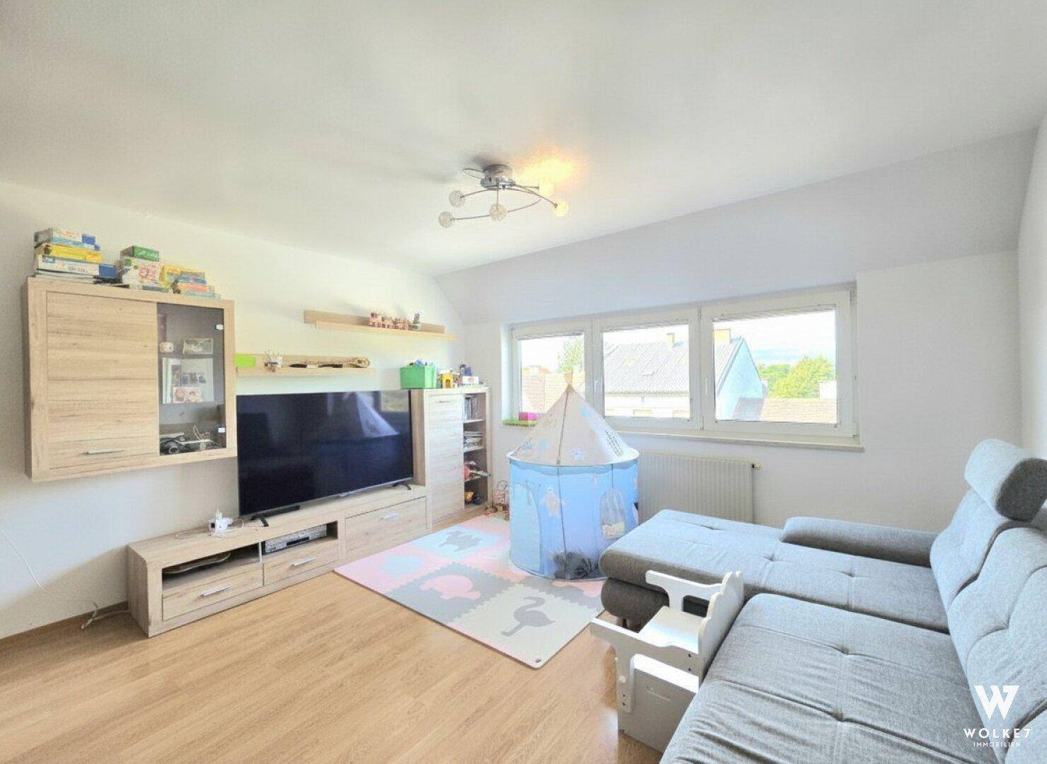 Helles Wohnzimmer mit grauem Ecksofa, TV-Möbel und einem Spielbereich für Kinder.