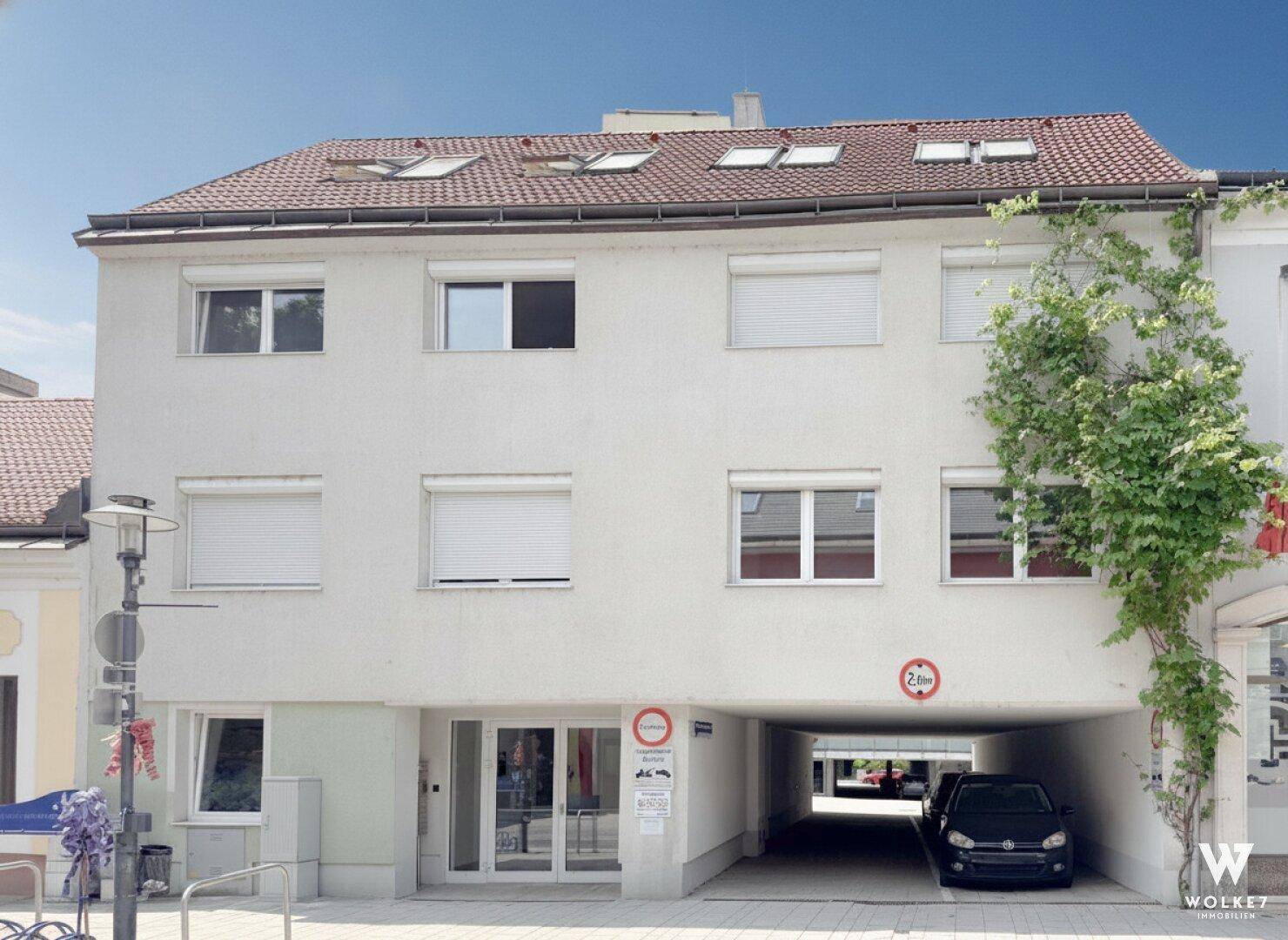 Vorderansicht des Wohnhauses mit weißer Fassade, Fenstern und einer Einfahrt zur Tiefgarage.