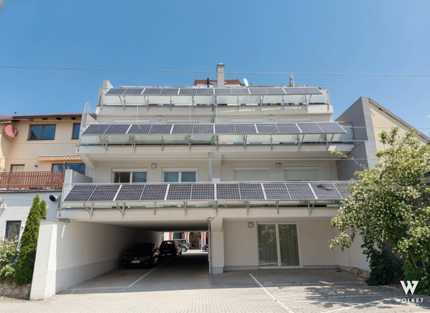 Moderne Rückfassade mit Balkonen, Glasgeländern und Photovoltaik-Anlage auf den Dächern.