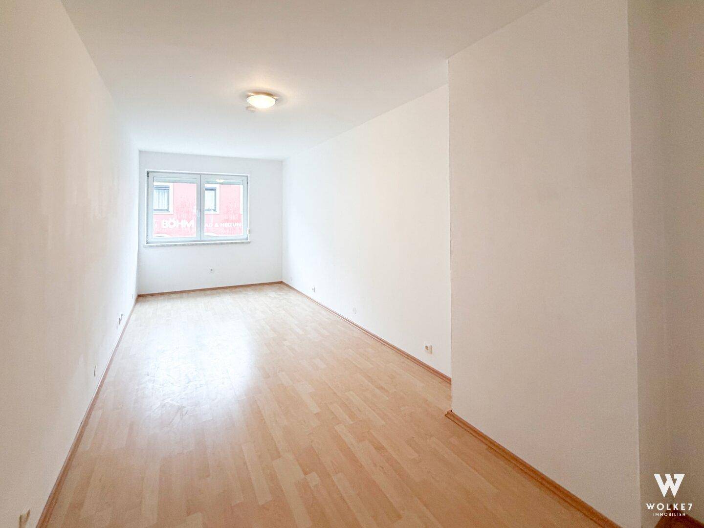 Leerer Raum mit hellem Laminatboden und einem Fenster mit Blick nach draußen.