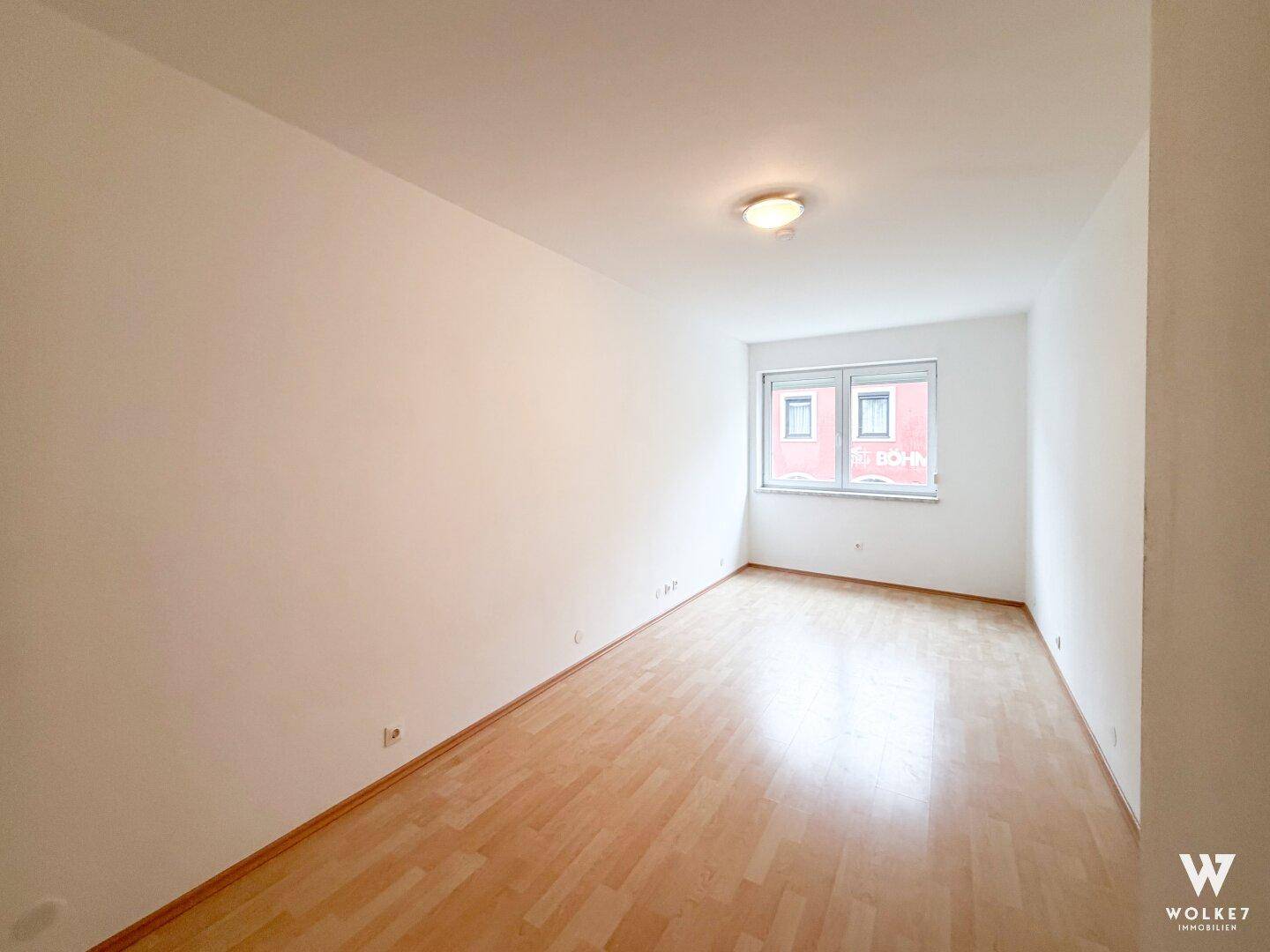 Heller, unmöblierter Raum mit Laminatboden und einem Fenster, das Tageslicht hereinlässt.