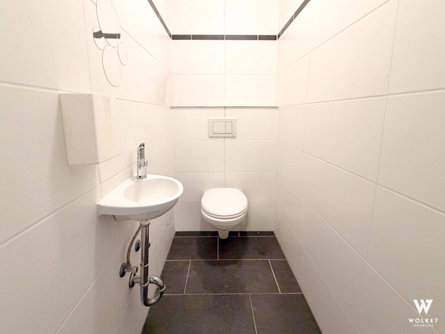 Modernes Gäste-WC mit weißen Fliesen, dunklem Boden und wandhängendem WC.