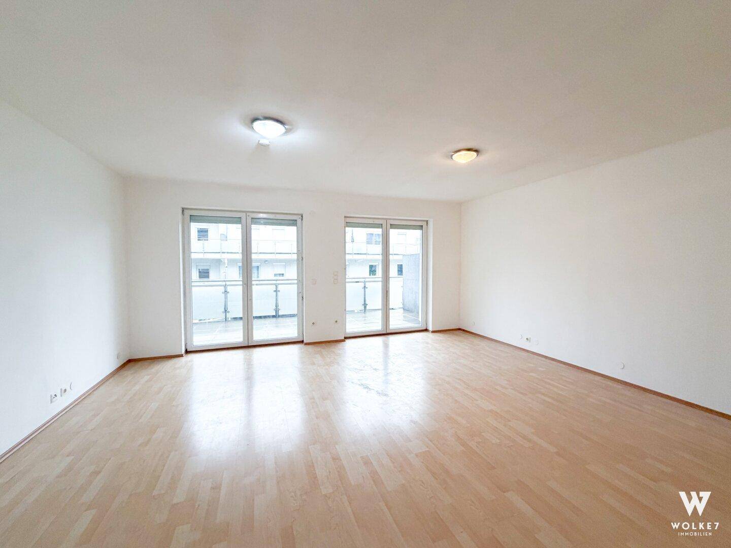 Geräumiger Wohnbereich mit hellem Laminatboden und Zugang zu einem Balkon.