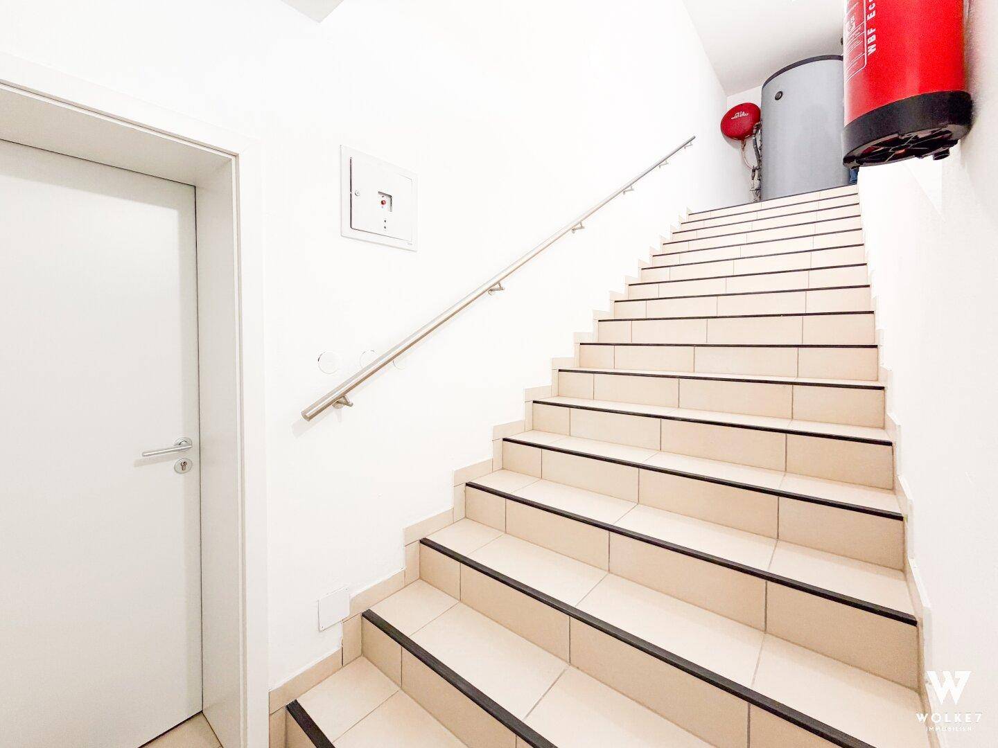 Helles Treppenhaus mit gefliesten Stufen, Handlauf und Brandschutzvorrichtungen.