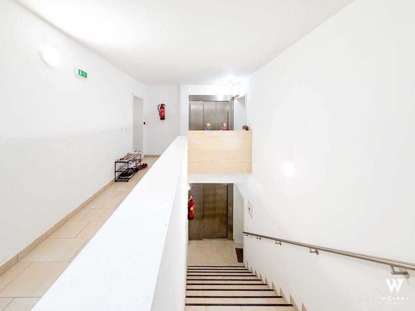Heller Flur mit Treppenhaus, Rampe und Zugang zu einem modernen Aufzug.