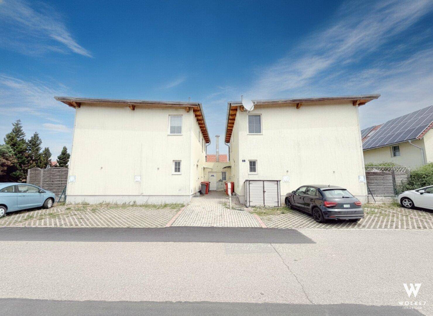 Zwei ähnliche Mehrfamilienhäuser mit heller Fassade und einem gemeinsamen Zufahrtsweg in der Mitte.