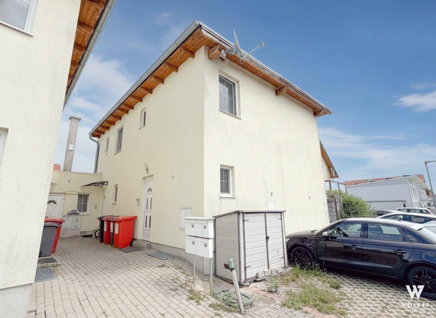 Eingangsbereich eines Mehrfamilienhauses mit Briefkästen, Mülltonnen und einem kleinen Geräteschuppen.