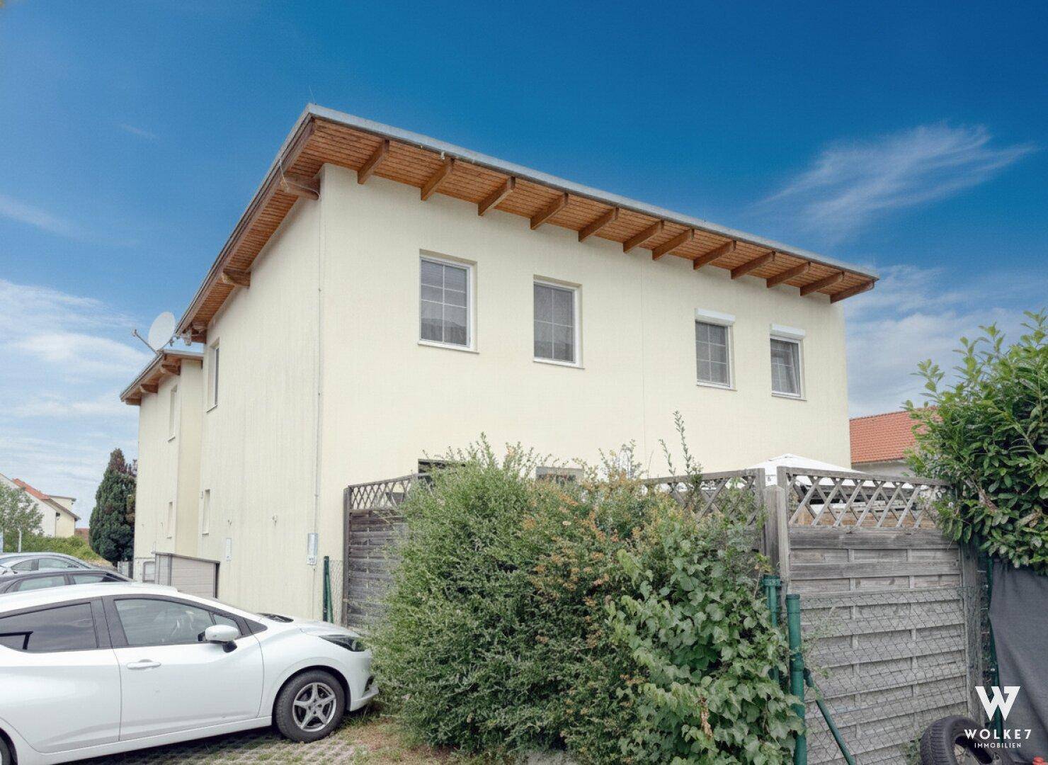 Rückansicht eines Mehrfamilienhauses mit heller Fassade, Holzsparren und einem grünen Zaun.