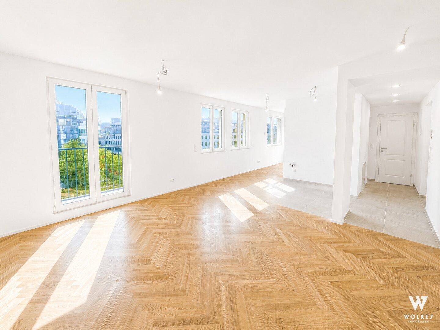 Geräumiges, leeres Wohnzimmer mit Fischgrätparkett, großen Fenstern und Balkonzugang.