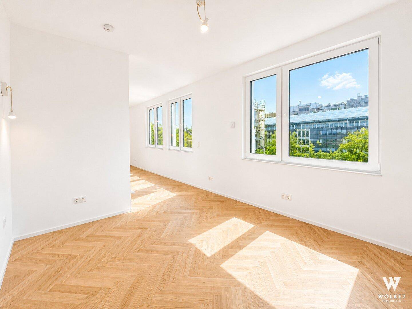 Helles, leeres Zimmer mit Fischgrätparkett und großen Fenstern, ideal als Wohn- oder Schlafzimmer.