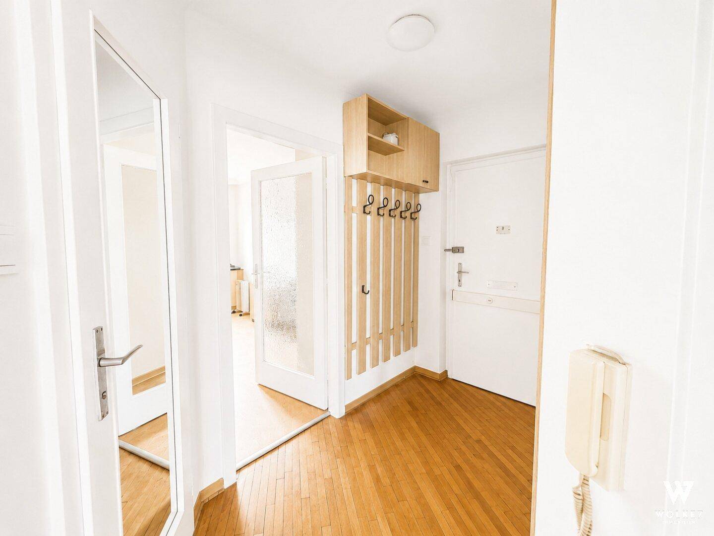 Heller Flur mit Holzparkett, Garderobe und Spiegel, der zu weiteren Räumen führt.