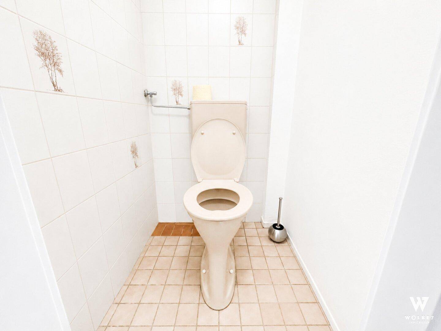 Separate Toilette mit hellen Fliesen und einem Fenster, in gutem, aber älterem Zustand.