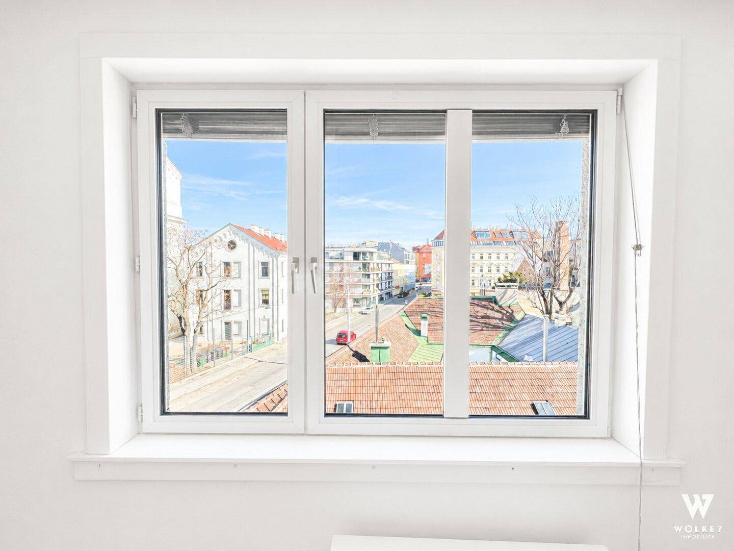 Fenster mit Blick auf die umliegende Stadtbebauung und Dächer bei sonnigem Wetter.