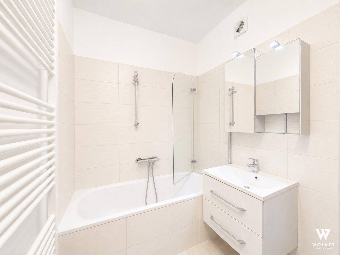 Modernes Badezimmer mit Badewanne, Duschabtrennung, Waschbecken und beheiztem Handtuchhalter.