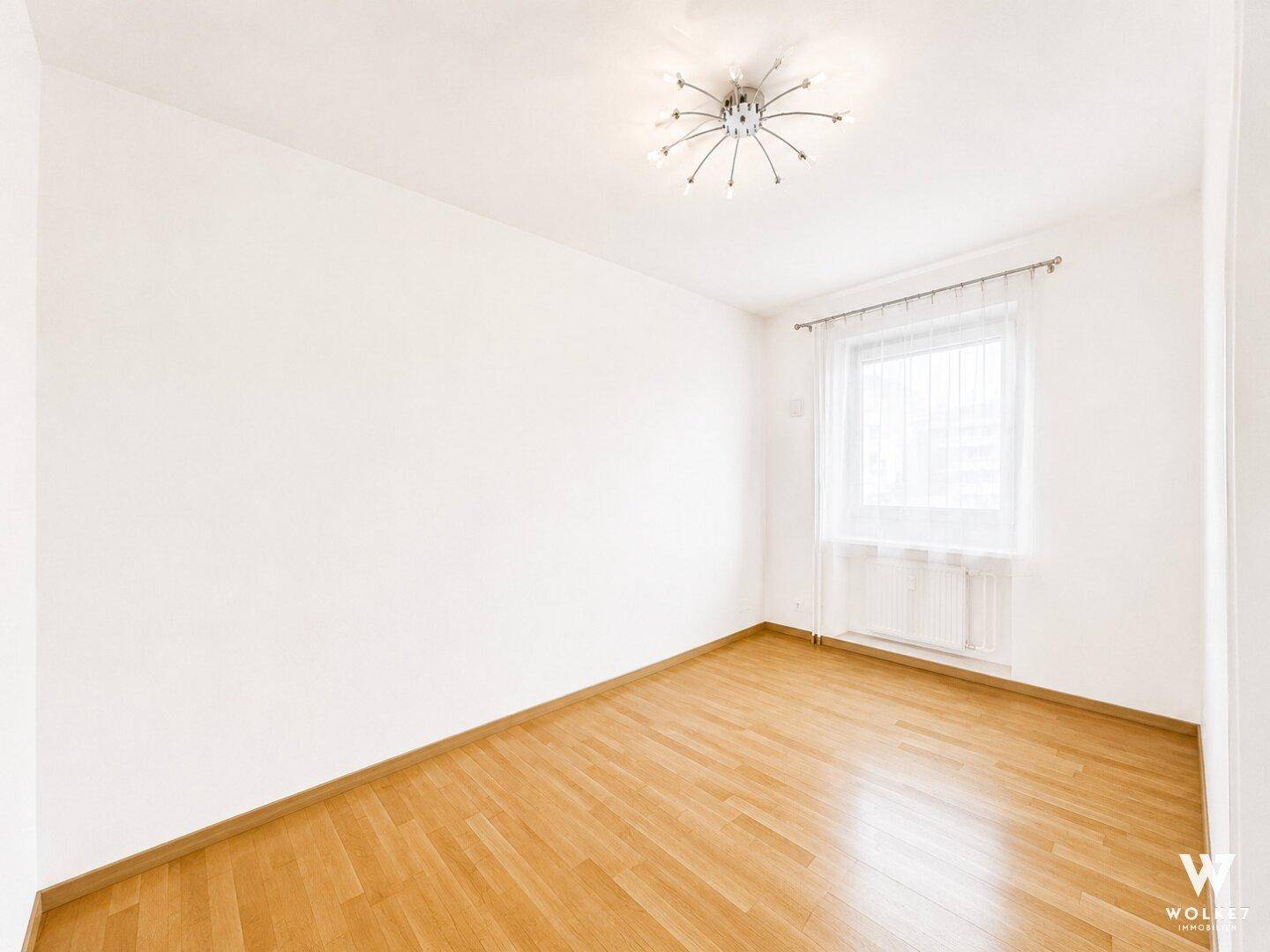 Leeres Zimmer mit Parkettboden und einem Fenster, das für ausreichend Helligkeit sorgt.