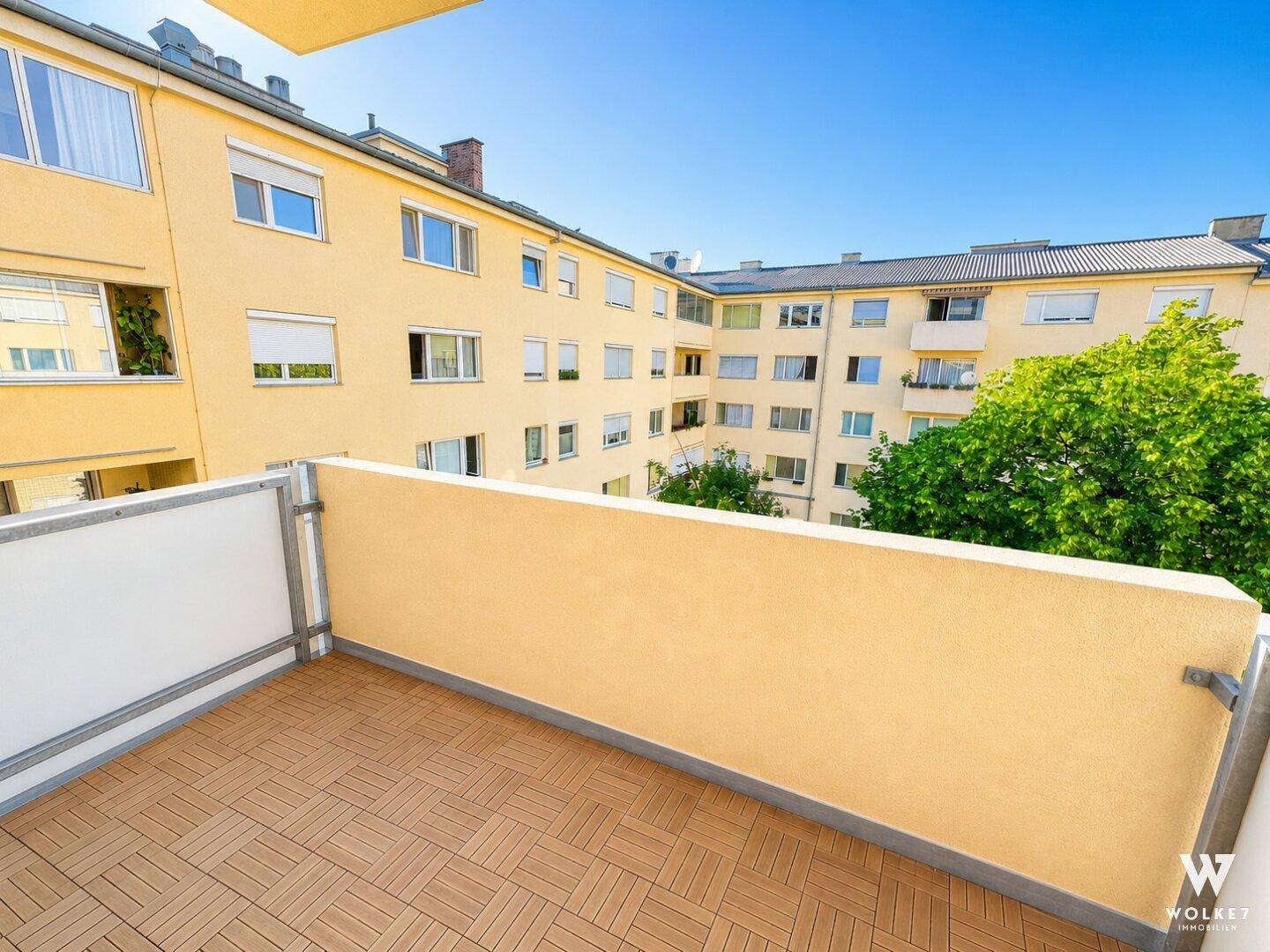 Heller Balkon mit Holzdielenboden und Blick auf die umliegenden Wohngebäude.