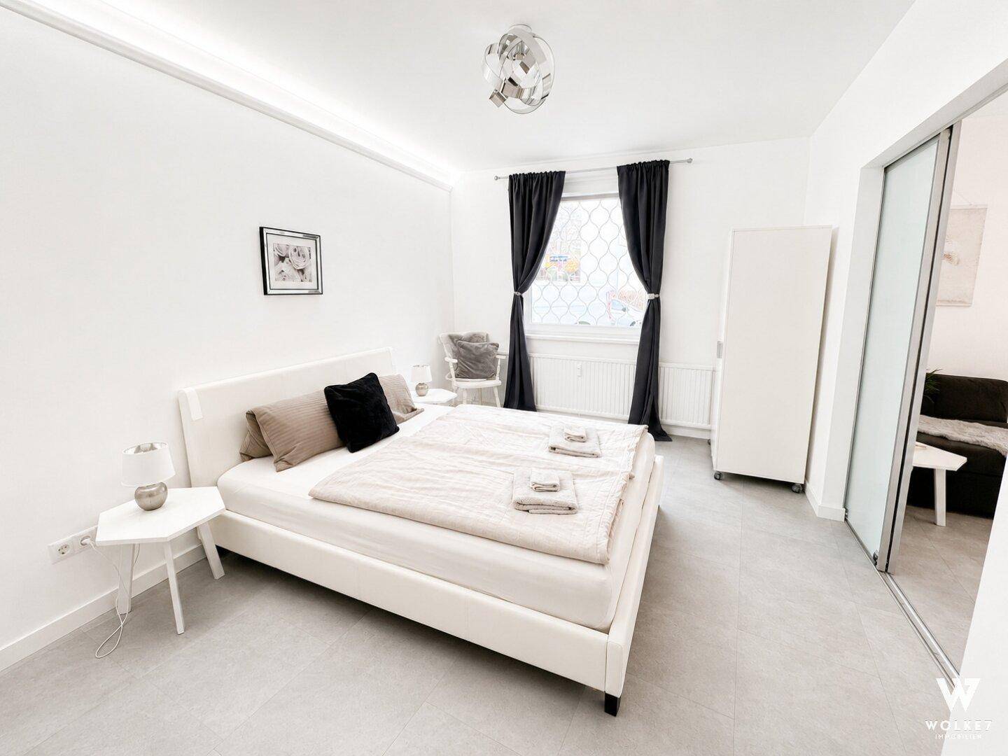 Geräumiges Schlafzimmer mit Bett, Kleiderschrank und Zugang zum Wohnbereich durch eine Schiebetür.