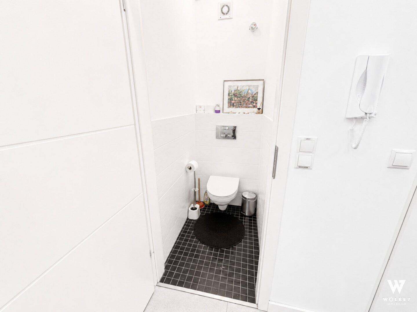 Kleines separates WC mit wandhängender Toilette und dunklen Bodenfliesen.