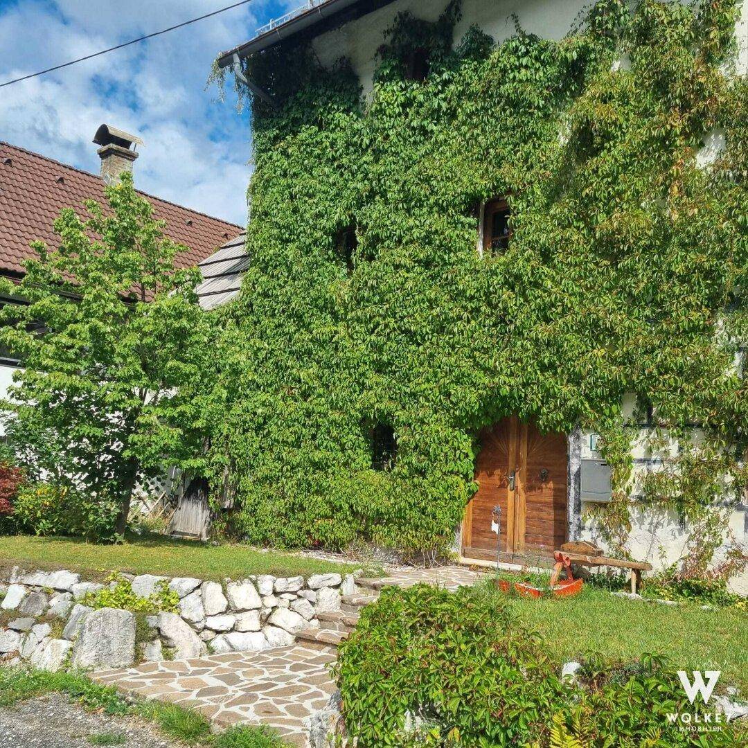 Fassade eines Gebäudes, dicht bewachsen mit Efeu, umgeben von üppigem Grün und einem Steinweg.