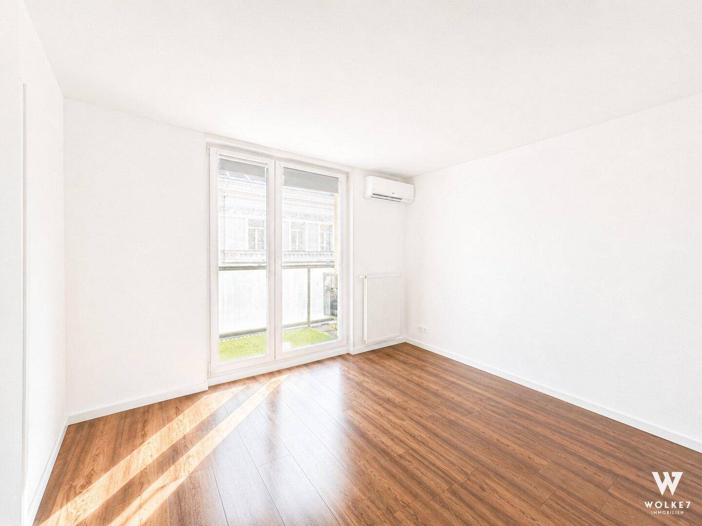 Unmöbliertes Schlafzimmer mit Holzboden, Klimaanlage und Zugang zu einem französischen Balkon.