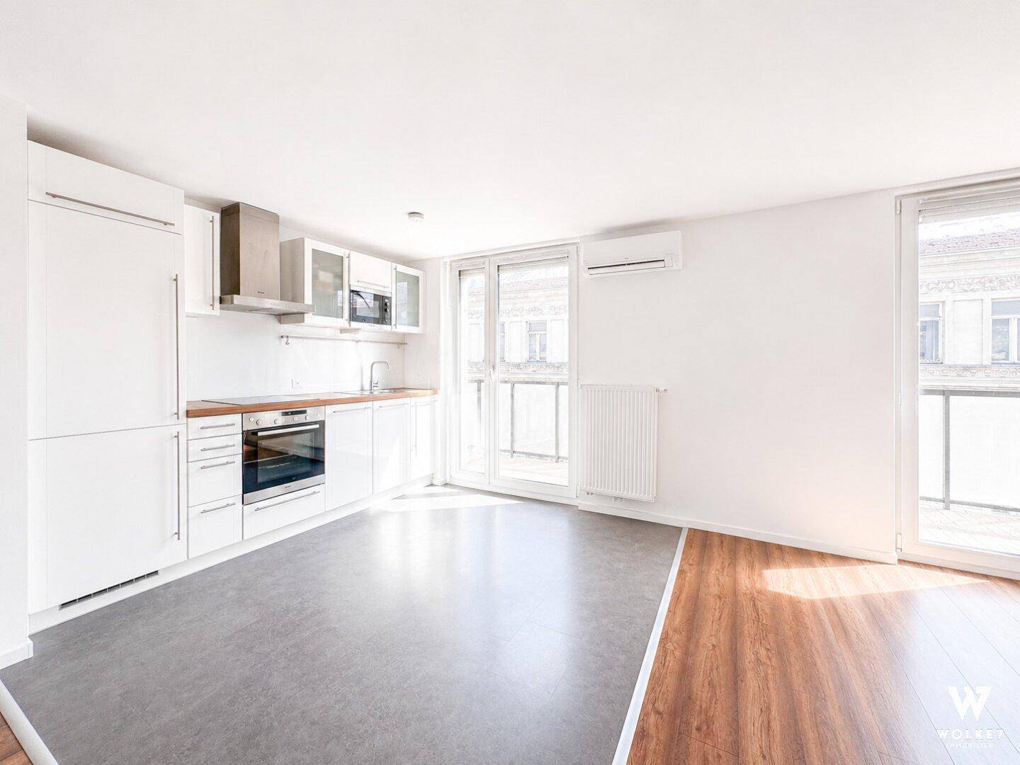 Moderne, unmöblierte Küche mit weißen Schränken, Einbaugeräten und Zugang zu einem französischen Balkon.