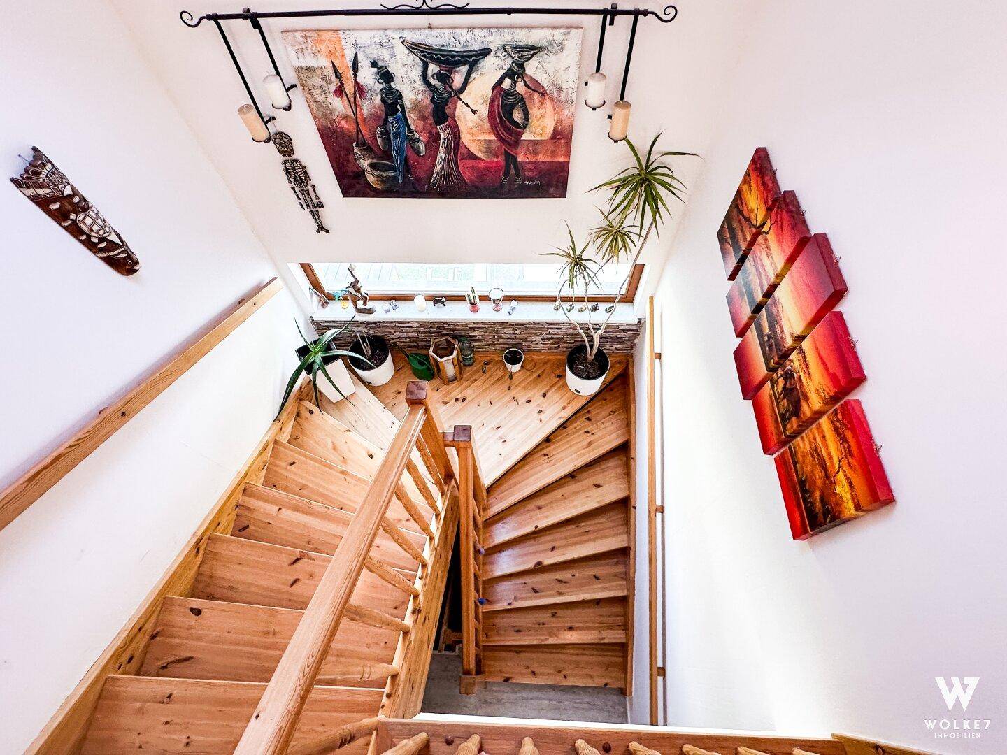 Holztreppe mit natürlichem Lichteinfall durch ein Dachfenster und dekorativen Kunstwerken.