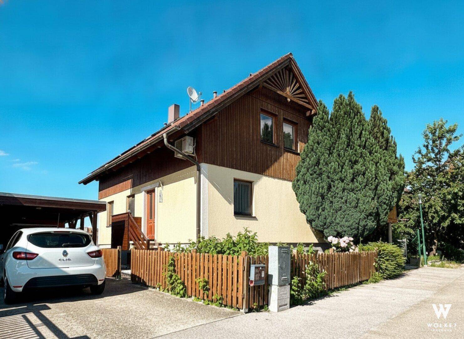 Vorderansicht des Hauses mit Carport, Holzzaun und gepflegter Einfahrt.