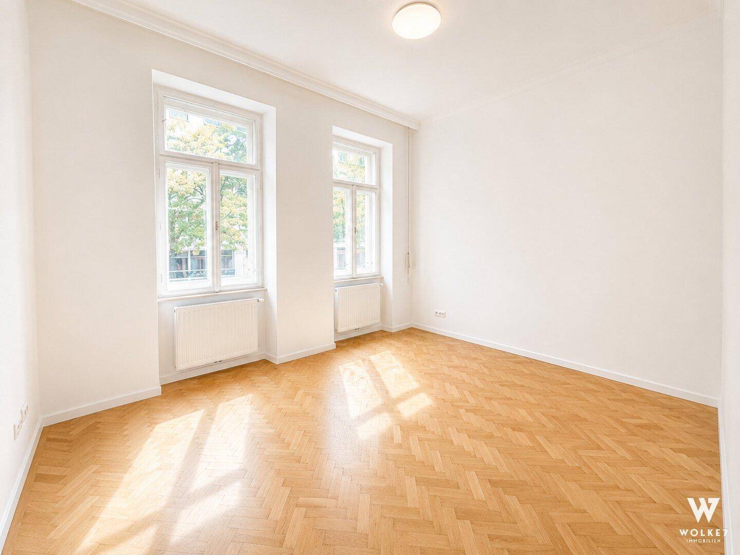 Leerer Raum mit Fischgrätparkett und großen Fenstern, bereit zur individuellen Gestaltung.