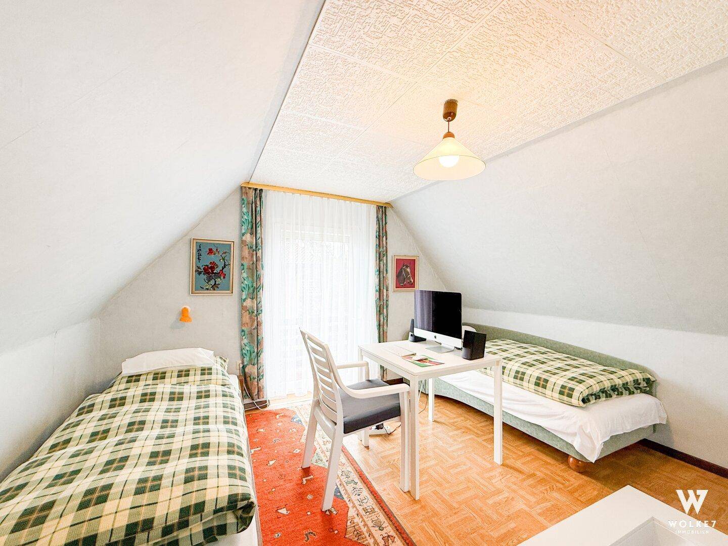 Helles Schlafzimmer im Dachgeschoss mit zwei Einzelbetten, Schreibtisch und schrägen Decken.