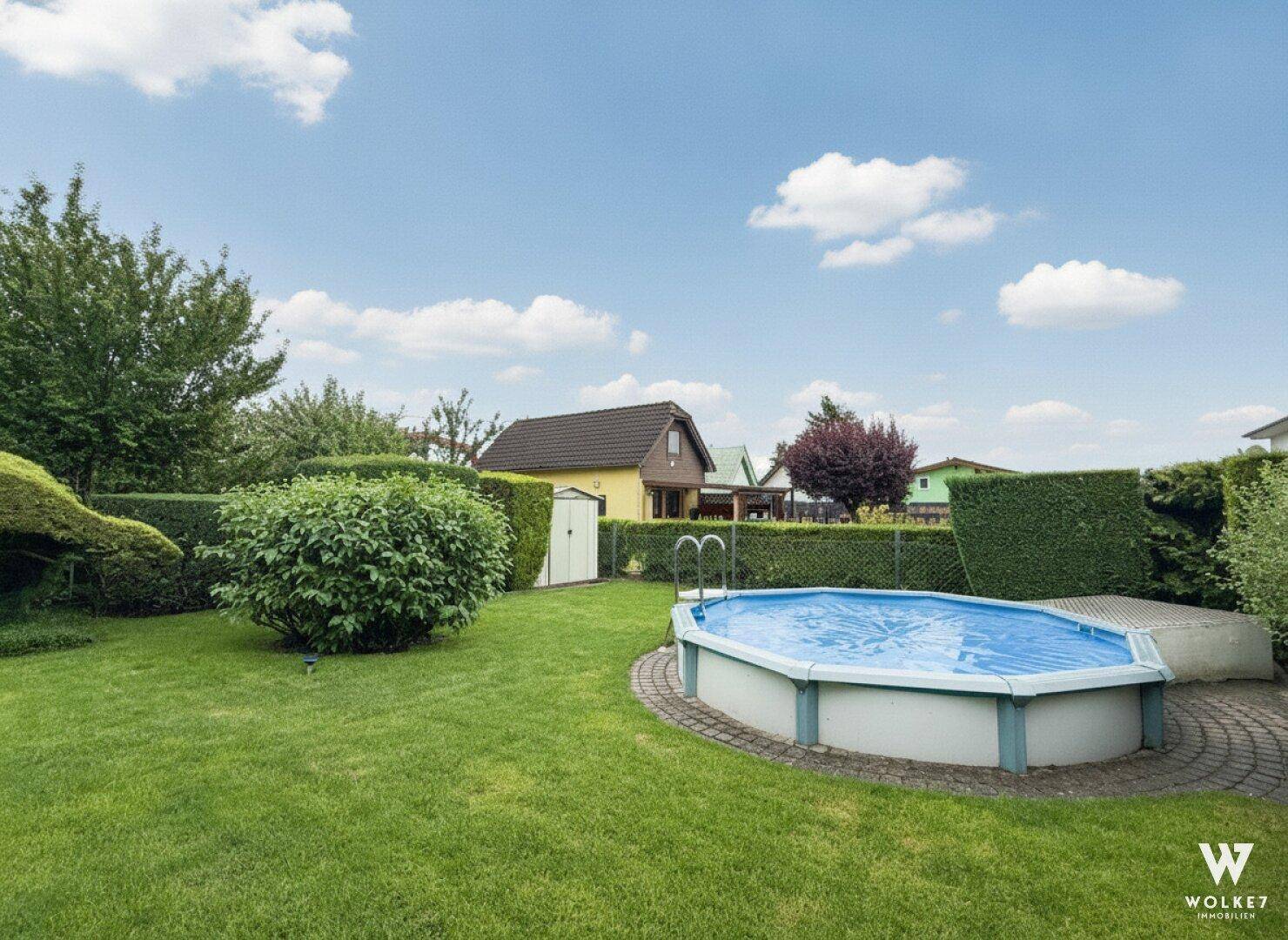 Großer Gartenbereich mit einem Aufstellpool und viel Grünfläche unter blauem Himmel.