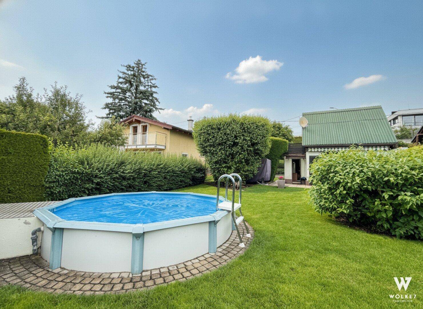 Weitläufiger Garten mit einem Aufstellpool, umgeben von Hecken und Bäumen.