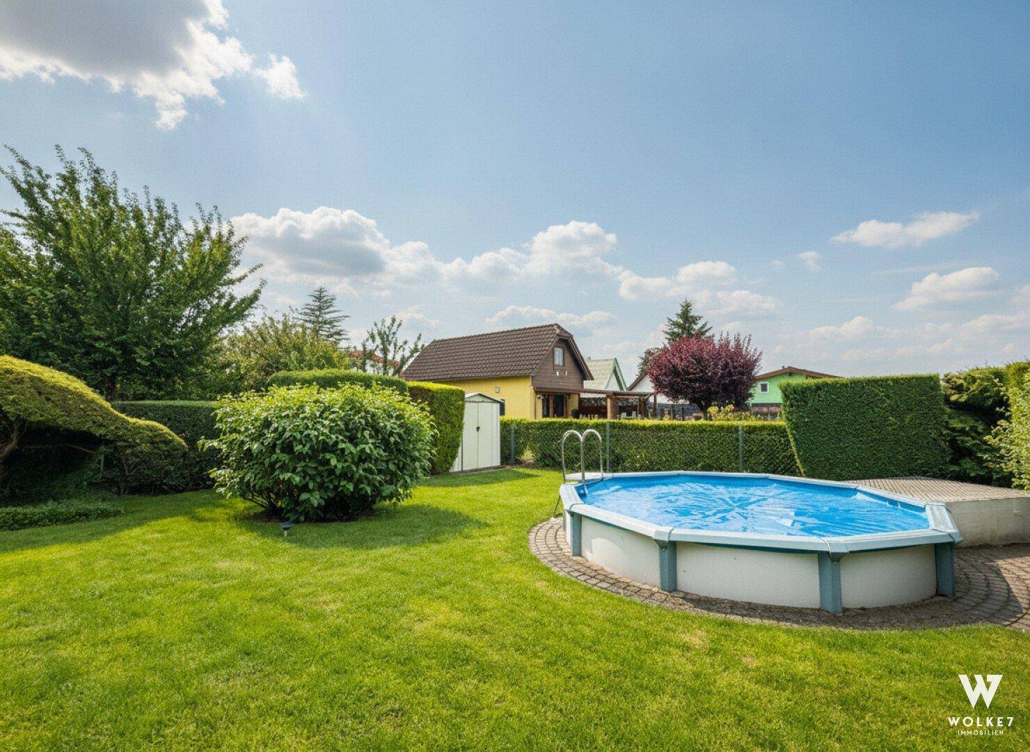Sonniger Gartenbereich mit einem Aufstellpool, umgeben von grünen Hecken und Bäumen.