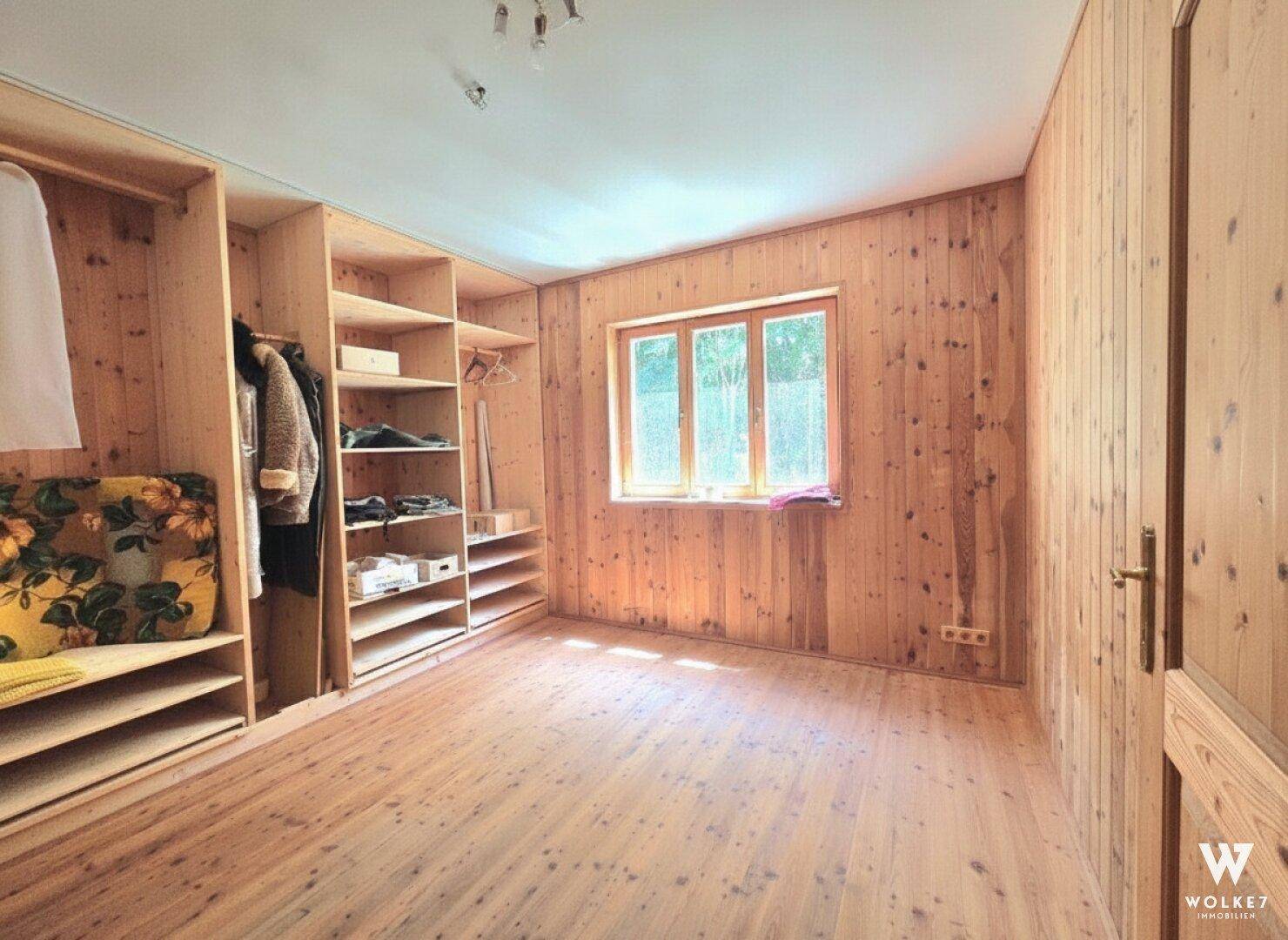 Schlafzimmer mit Holzwänden, Einbauschränken und Fenster, das viel Licht spendet.