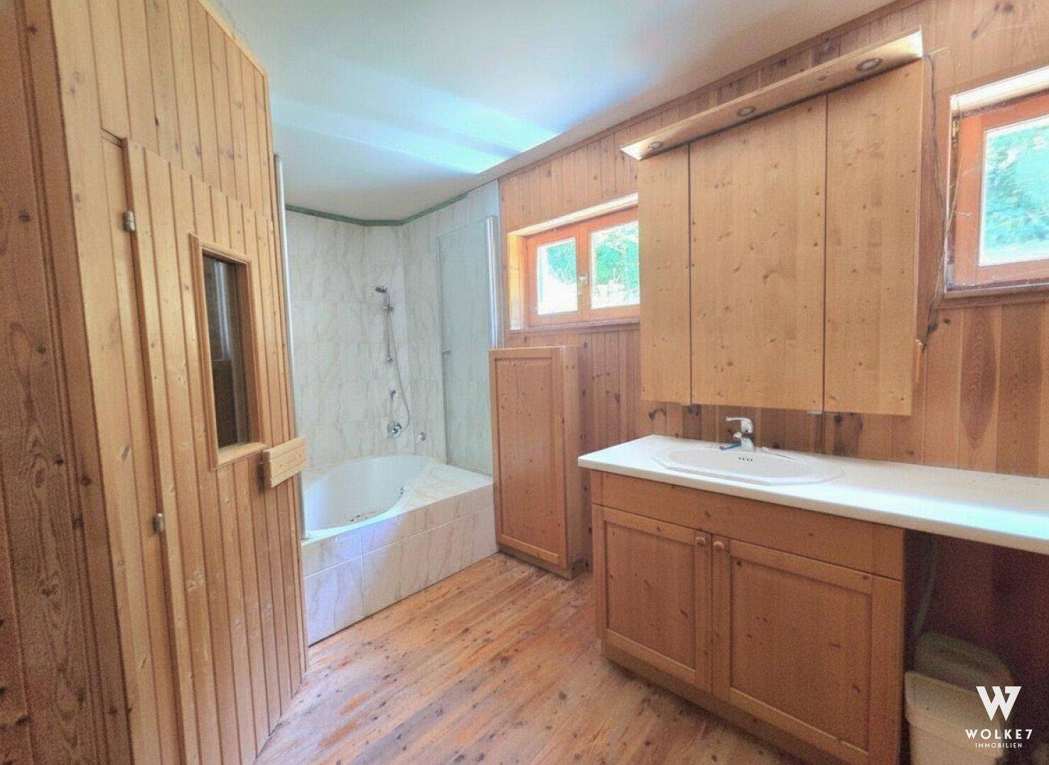 Badezimmer mit Holzwänden, Badewanne, Einzelwaschbecken und integrierter Sauna.