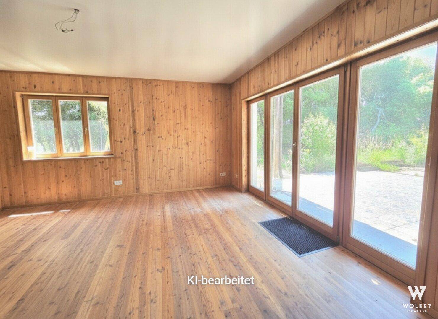 Geräumiges Wohnzimmer mit Holzboden und großen Fenstern, die viel Tageslicht hereinlassen.