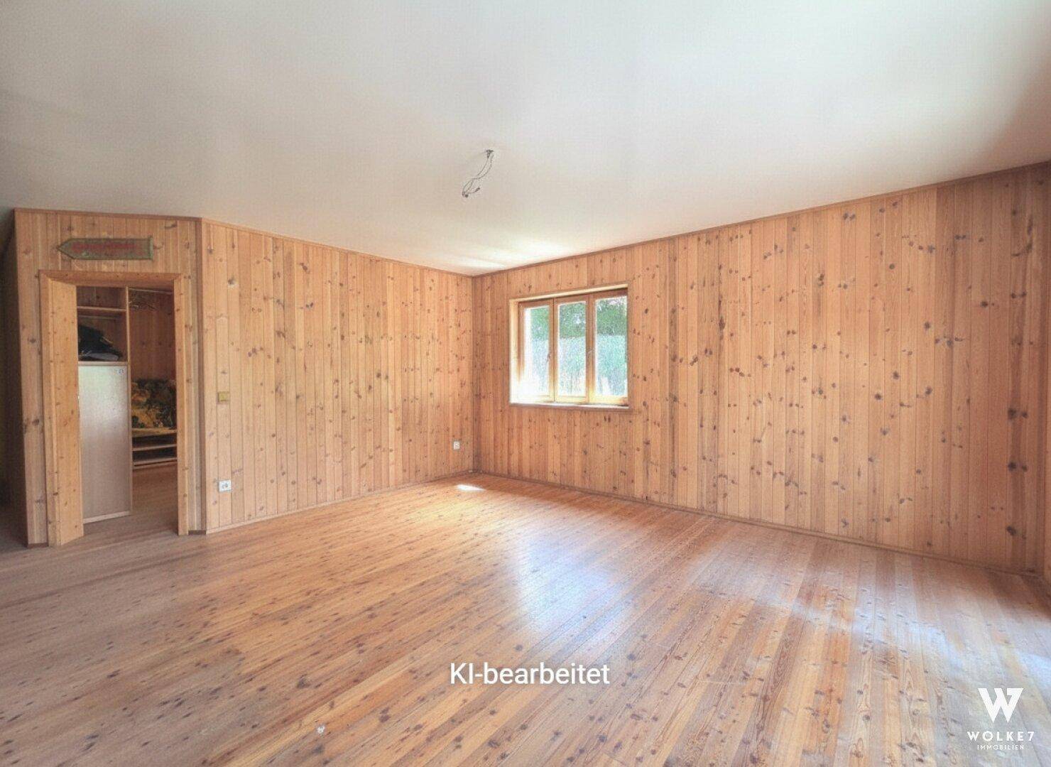 Heller Raum mit Holzwänden und -boden, einem Fenster und Zugang zu einem Schrankbereich.