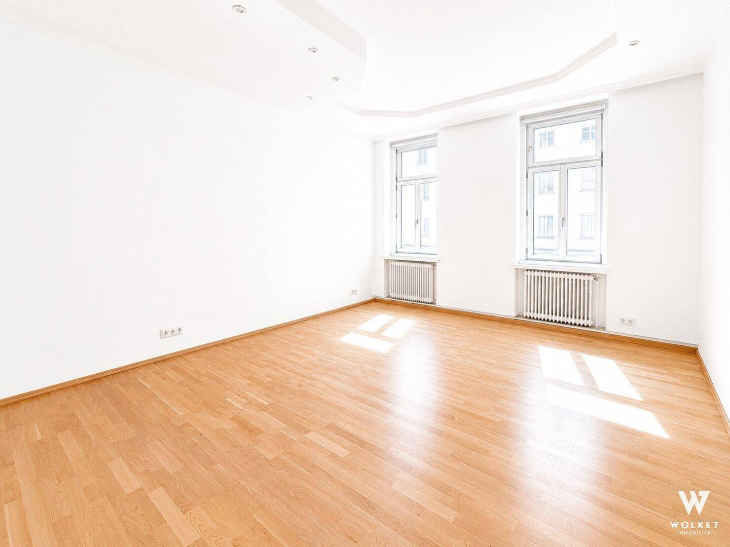 Heller, leerer Raum mit Holzboden und zwei großen Fenstern, bietet vielseitige Nutzungsmöglichkeiten.