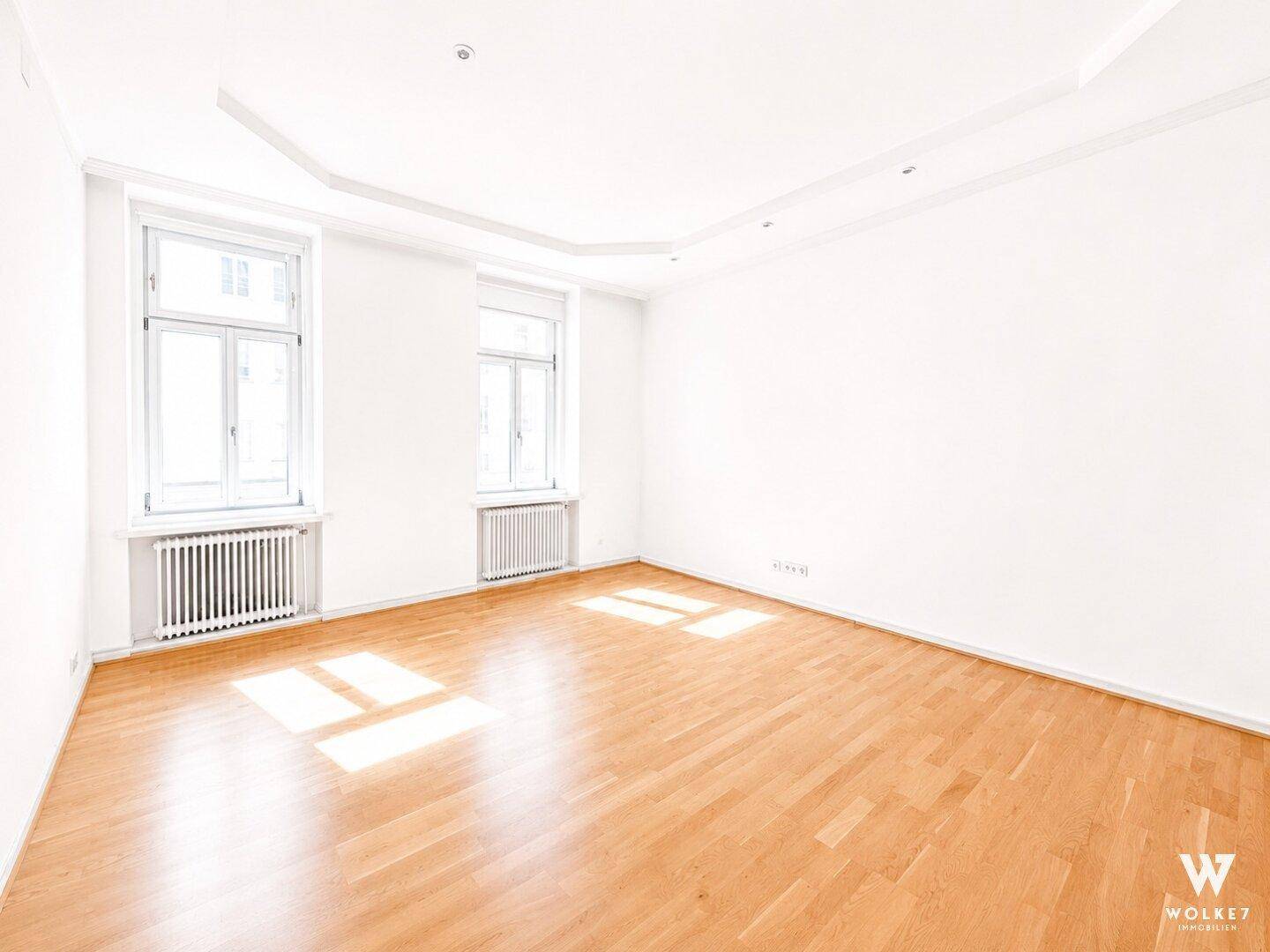 Geräumiger, unmöblierter Raum mit Holzboden und großen Fenstern, ideal für Wohn- oder Schlafzimmer.