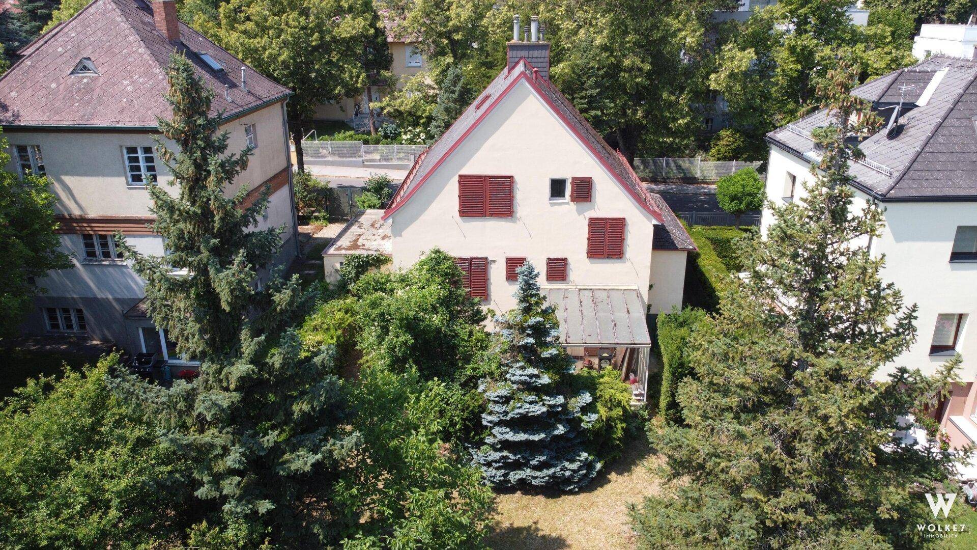 Luftaufnahme des Hauses mit angrenzenden Nachbargebäuden und einem großen, grünen Gartenbereich mit Bäumen.