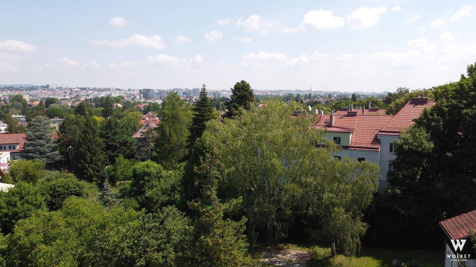 Panoramablick über eine grüne Wohngegend mit vielen Bäumen und Gebäuden in der Ferne an einem sonnigen Tag.