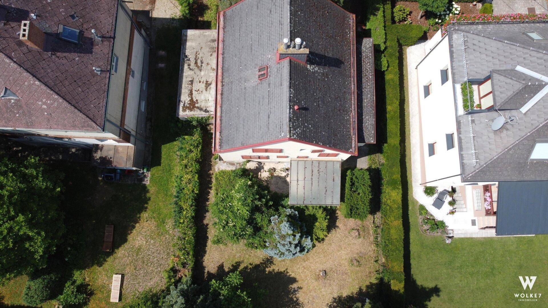 Draufsicht auf das Haus und das Grundstück mit Garten, umgeben von Hecken und benachbarten Gebäuden.